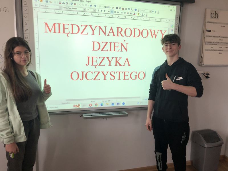 Uczennica i uczeń przy tablicy z napisem MIĘDZYNARODOWY DZIEŃ JĘZYKA OJCZYSTEGO